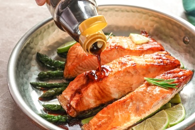 Pouring sauce onto tasty cooked salmon in frying pan, closeup