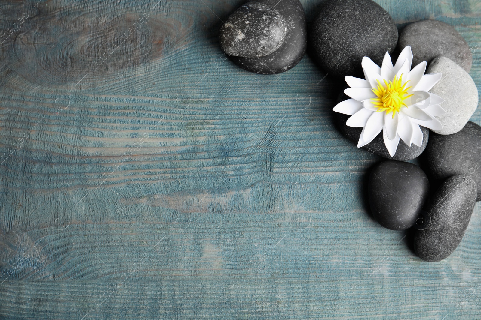 Photo of Stones with lotus flower and space for text on blue wooden background, flat lay. Zen lifestyle