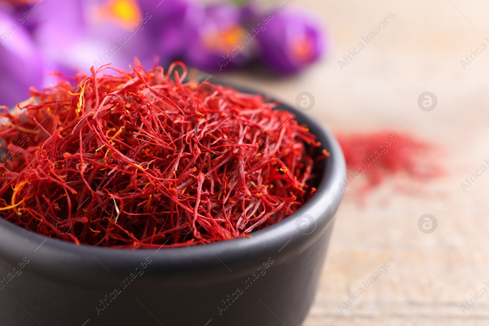 Photo of Dried saffron in bowl and crocus flowers on table, closeup