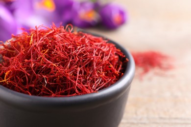 Photo of Dried saffron in bowl and crocus flowers on table, closeup