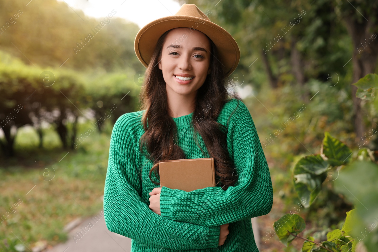 Photo of Beautiful young woman in stylish warm sweater with book outdoors