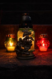 Photo of Different grave lanterns with burning candles on stone surface at night