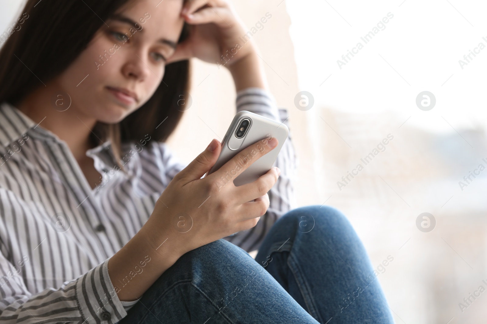 Photo of Young woman holding mobile phone on light background, closeup with space for text. Loneliness concept