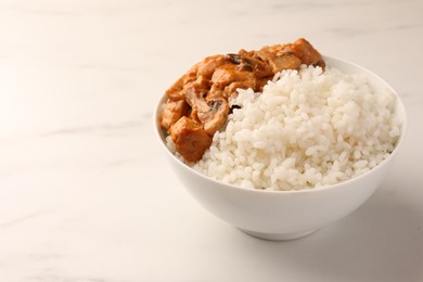 Bowl of delicious rice with meat and mushrooms on white marble table, space for text