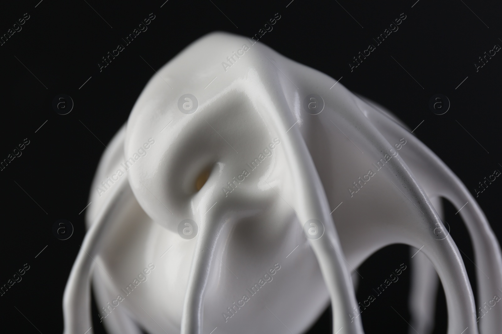 Photo of Whisk with whipped cream on black background, closeup