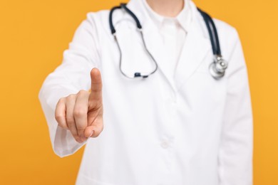 Doctor with stethoscope pointing on orange background, closeup