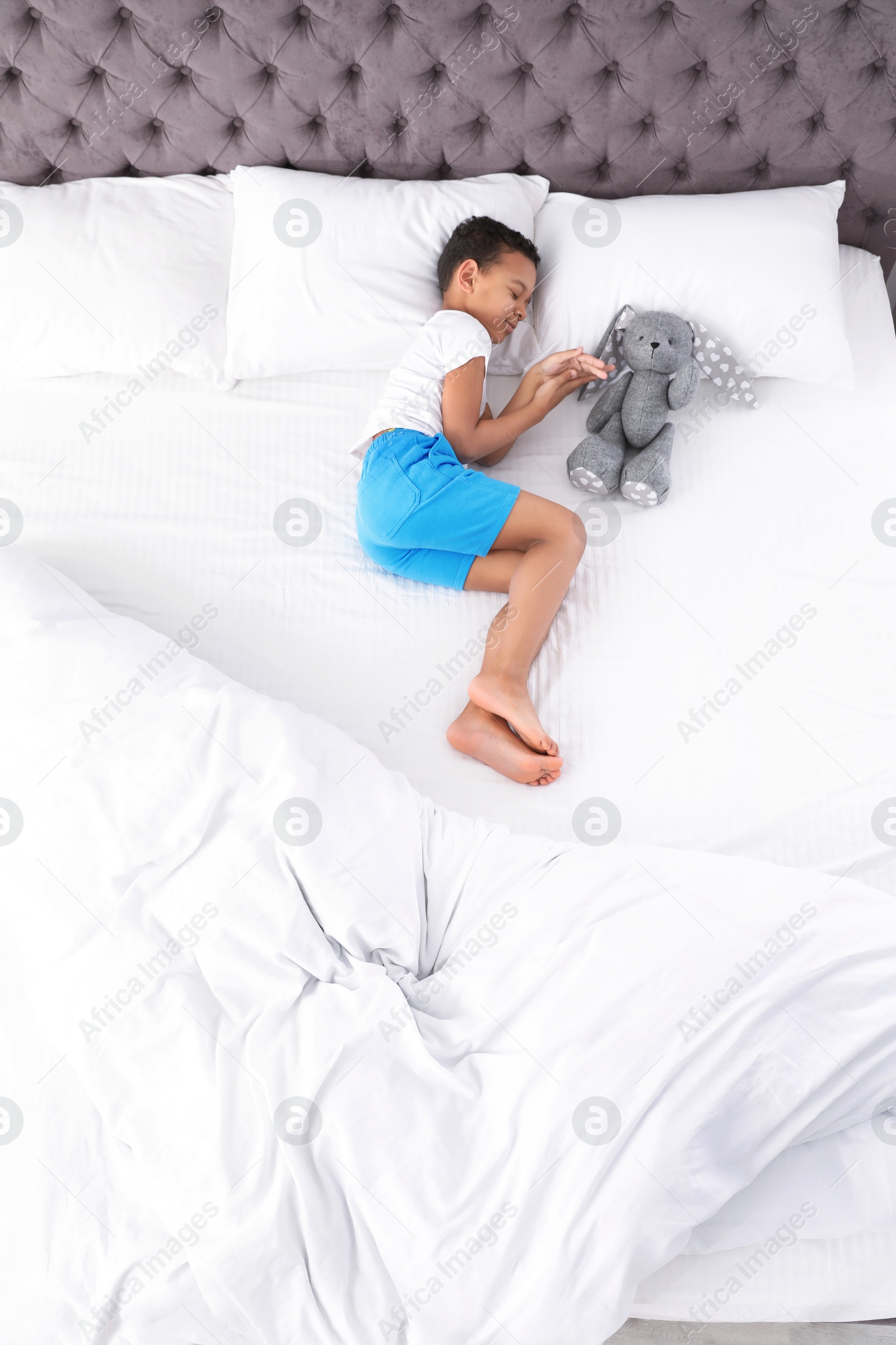 Photo of Cute little African-American boy with toy rabbit sleeping in bed, top view