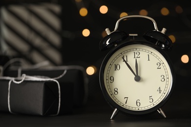 Photo of Vintage alarm clock with decor on black table against blurred Christmas lights, closeup. New Year countdown