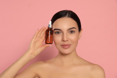 Young woman with bottle of essential oil on pink background
