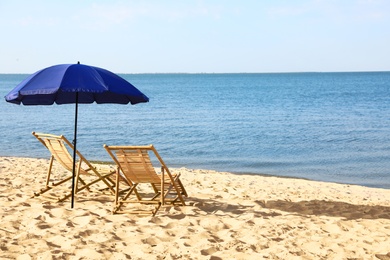 Photo of Empty wooden sunbeds and umbrella on sandy shore. Beach accessories