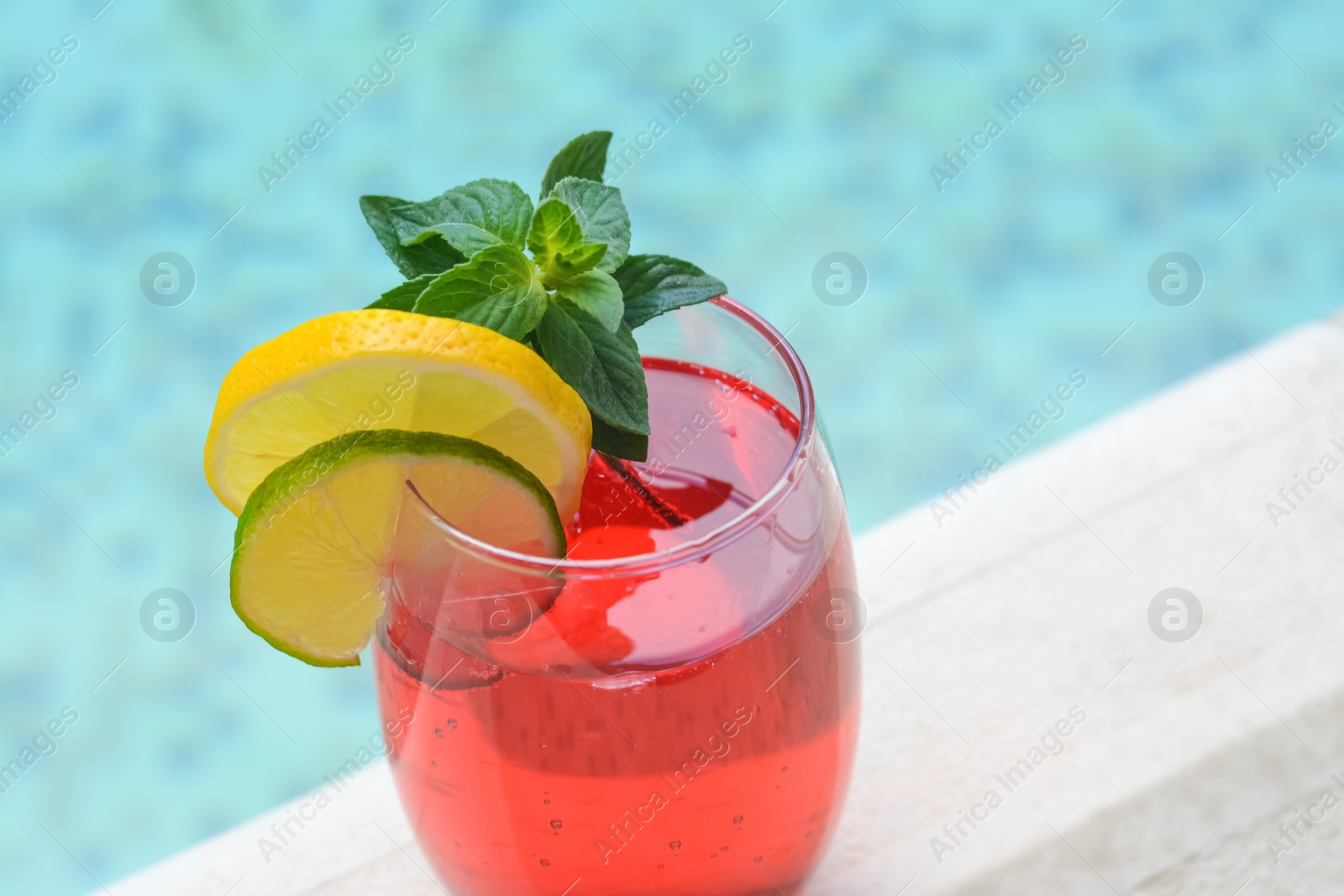 Photo of Glass of delicious cocktail near swimming pool, closeup. Refreshing drink