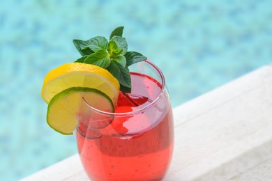 Photo of Glass of delicious cocktail near swimming pool, closeup. Refreshing drink