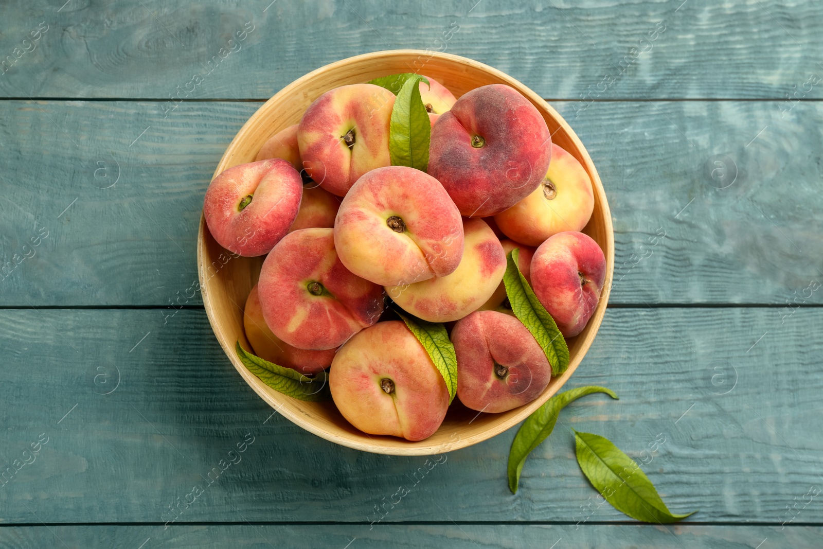 Photo of Fresh ripe donut peaches on light blue wooden table, top view