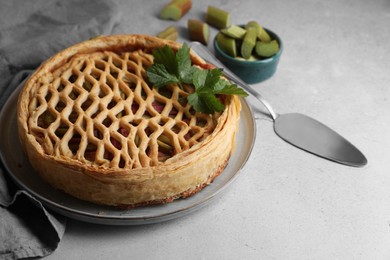 Freshly baked rhubarb pie, cut stalks and cake server on light grey table