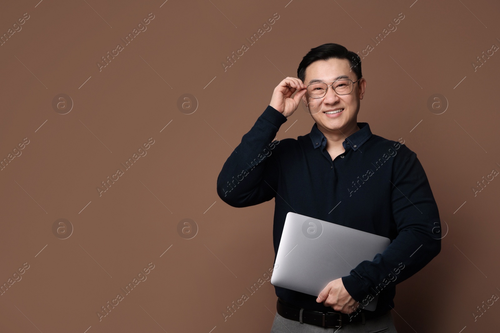 Photo of Portrait of happy man with laptop on brown background. Space for text