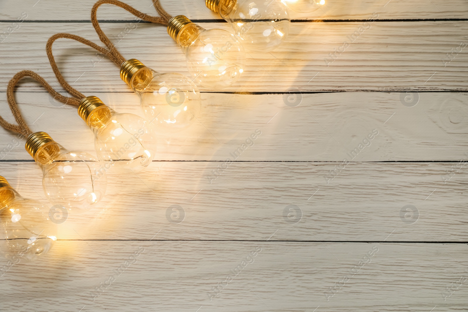 Photo of String lights with lamp bulbs on wooden background, top view. Space for text