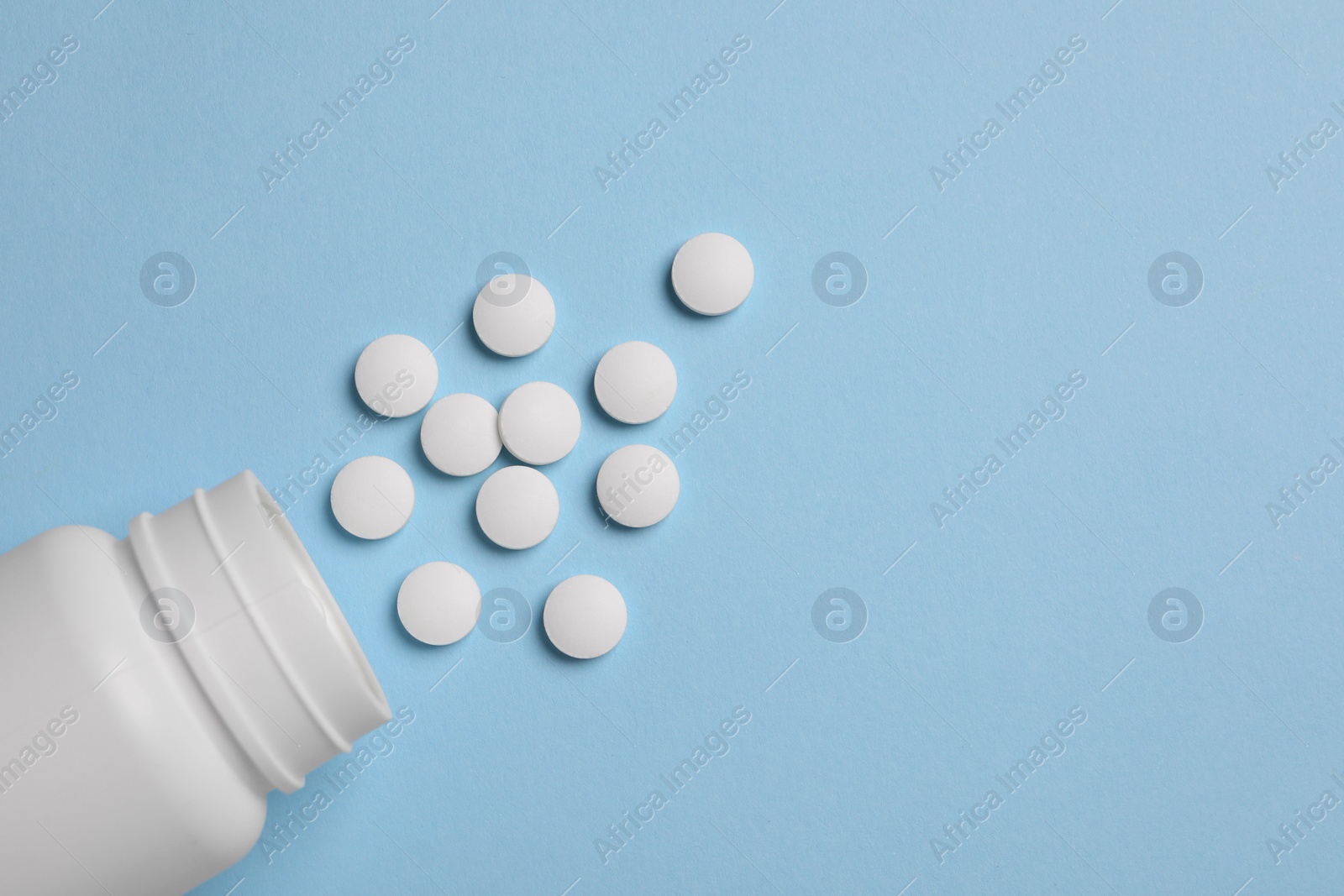 Photo of Plastic medical bottle with pills on light blue background, flat lay. Space for text