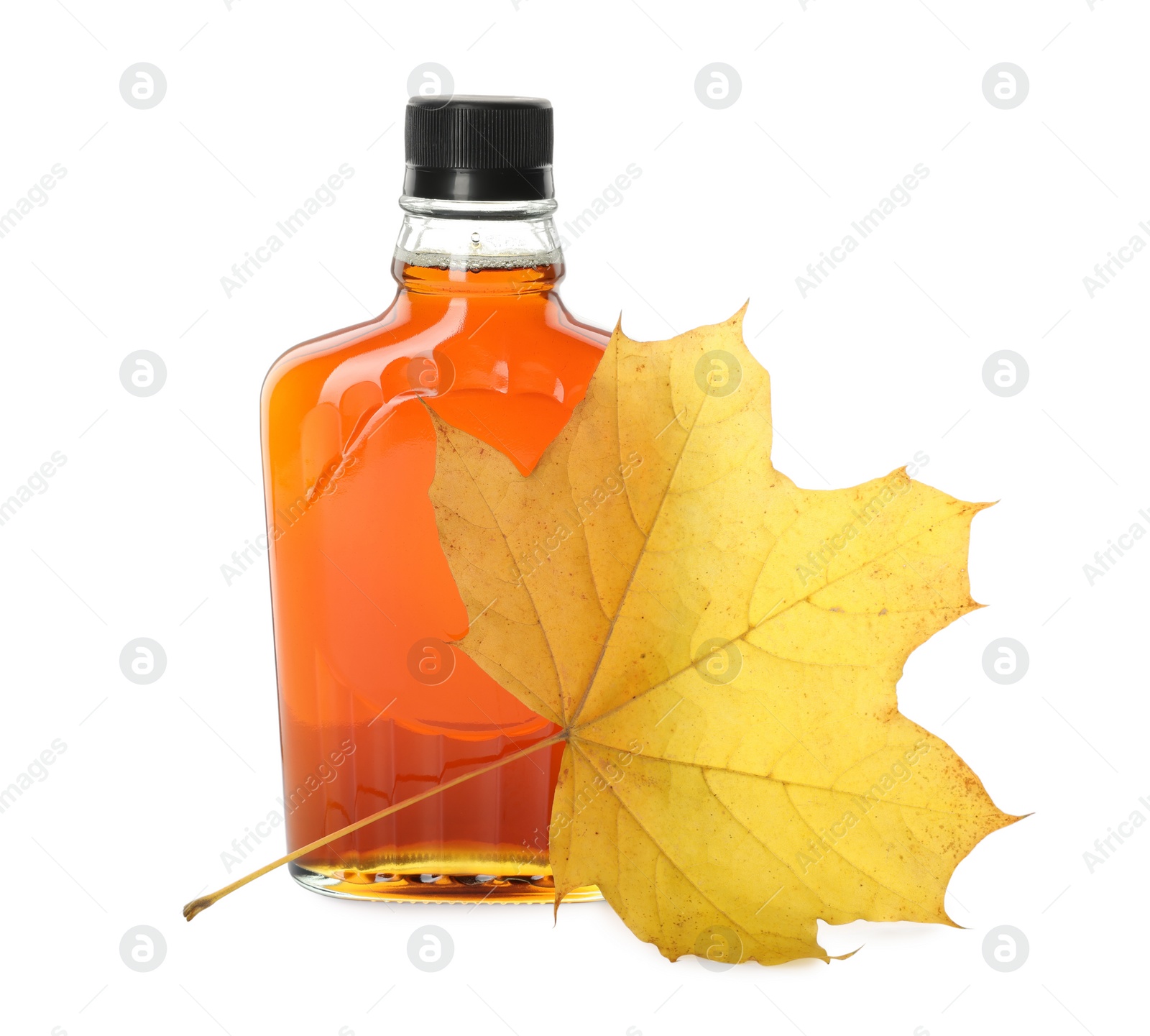 Photo of Bottle of tasty maple syrup and dry leaf on white background