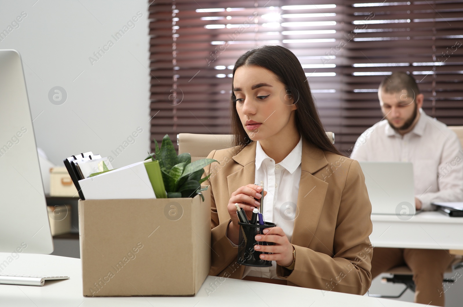 Photo of Dismissed woman packing personal stuff into box in office