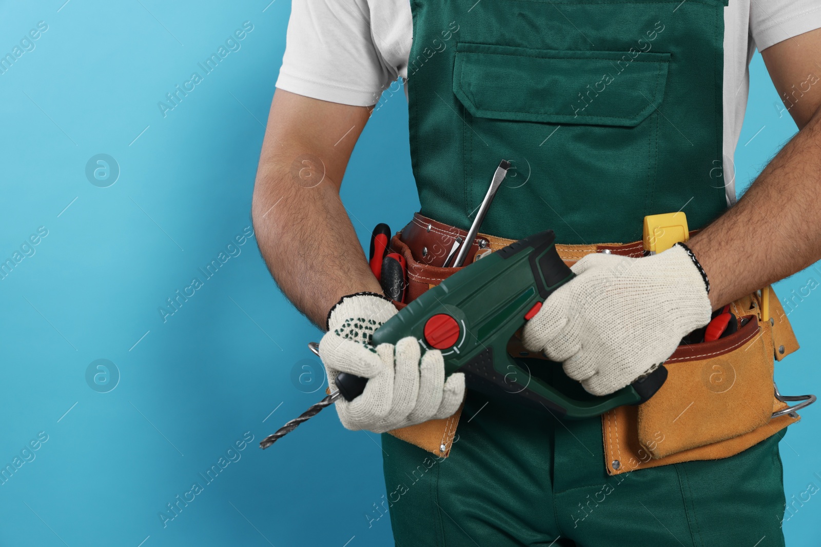 Photo of Worker in uniform with power drill on light blue background, closeup. Space for text