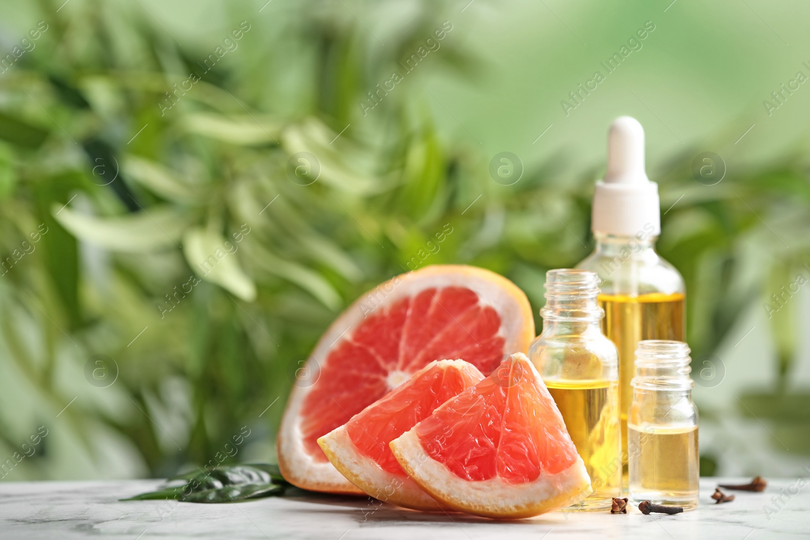 Photo of Bottles of essential oil and grapefruit slices on table against blurred background. Space for text