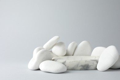 Photo of Presentation for product. Stone podium and pebbles on light grey background. Space for text