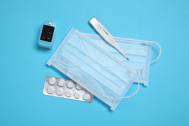 Photo of Flat lay composition with thermometer, pills and medical masks on light blue background