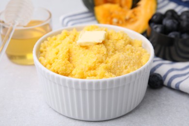 Photo of Tasty cornmeal with butter in bowl on light gray table, closeup