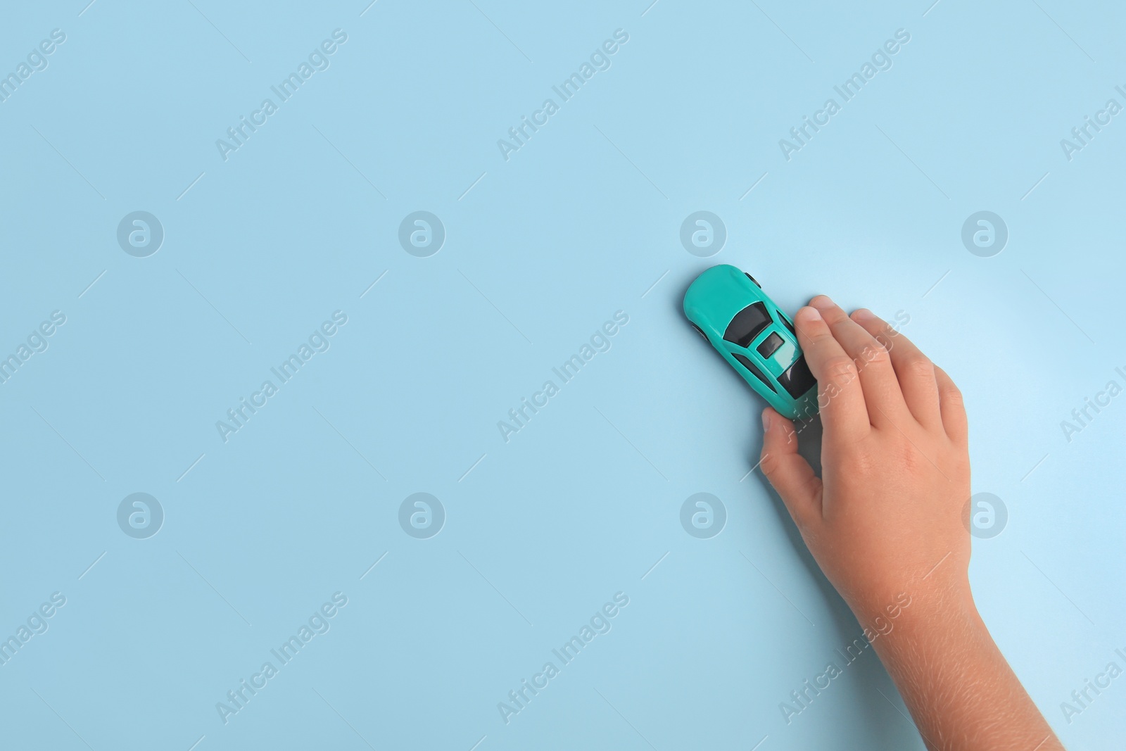 Photo of Child playing with toy car on light blue background, top view. Space for text