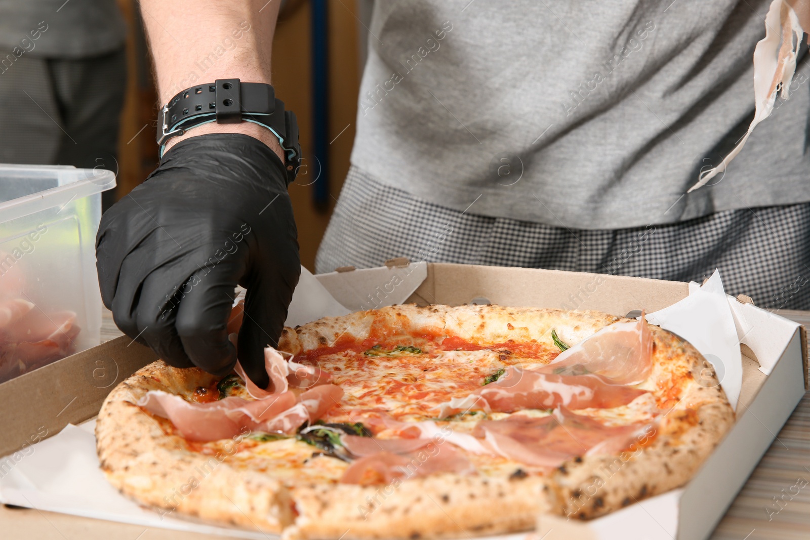 Photo of Professional chef adding prosciutto to Italian oven baked pizza in restaurant, closeup