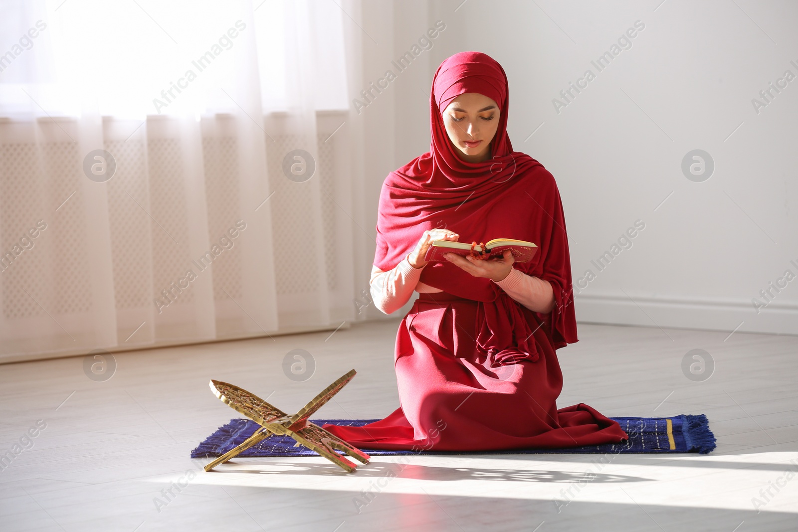 Photo of Muslim woman in hijab reading Koran indoors