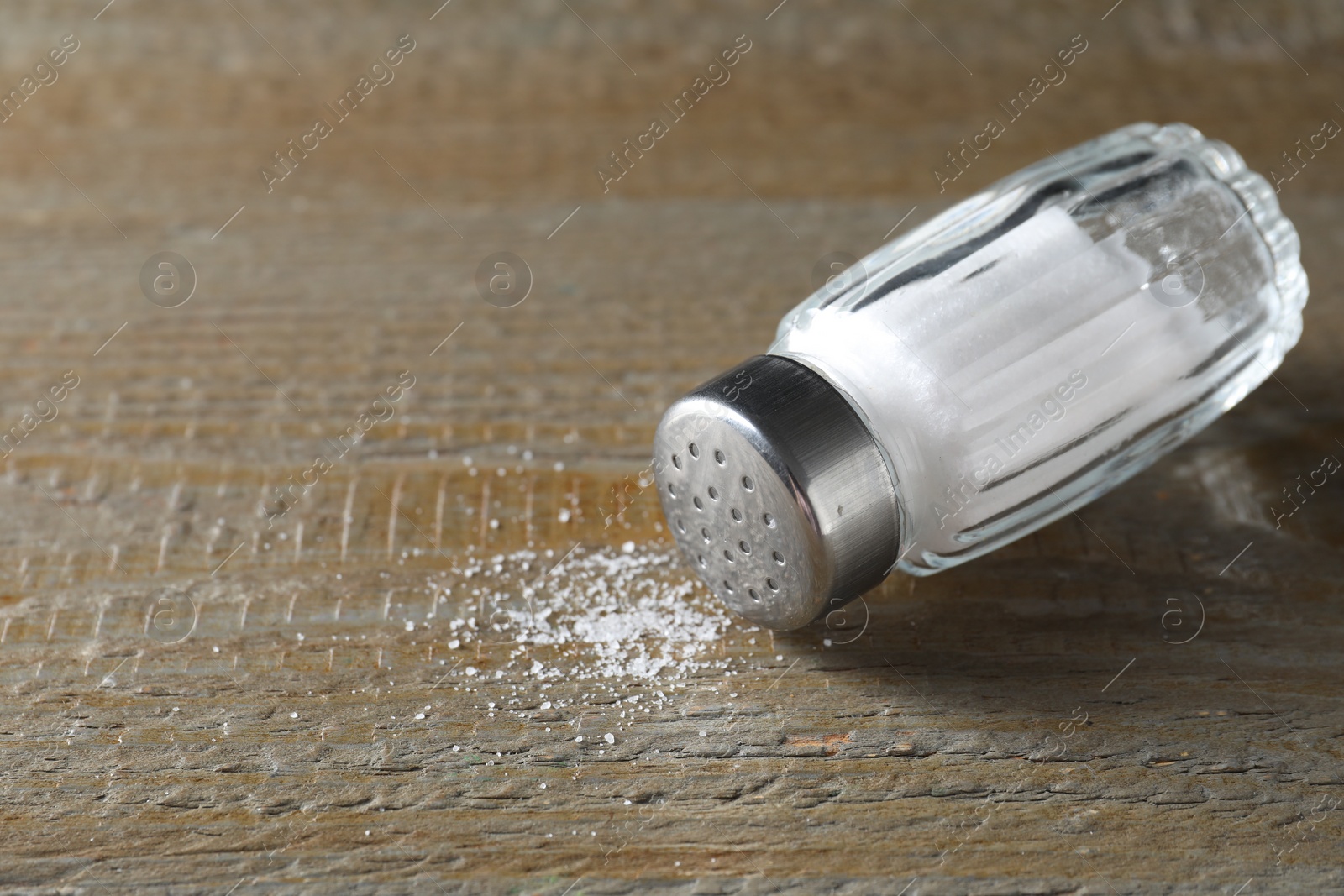 Photo of Organic salt in glass shaker on wooden table, closeup. Space for text