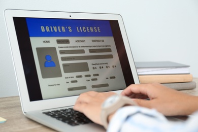 Photo of Woman using laptop to fill driver's license application form at table in office, closeup