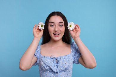 Beautiful woman with spring flowers in hands on light blue background