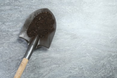 Photo of Metal shovel with fertile soil on gray textured surface, top view. Space for text