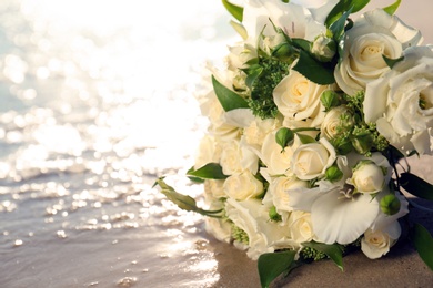 Photo of Beautiful wedding bouquet on sandy beach near sea, closeup. Space for text