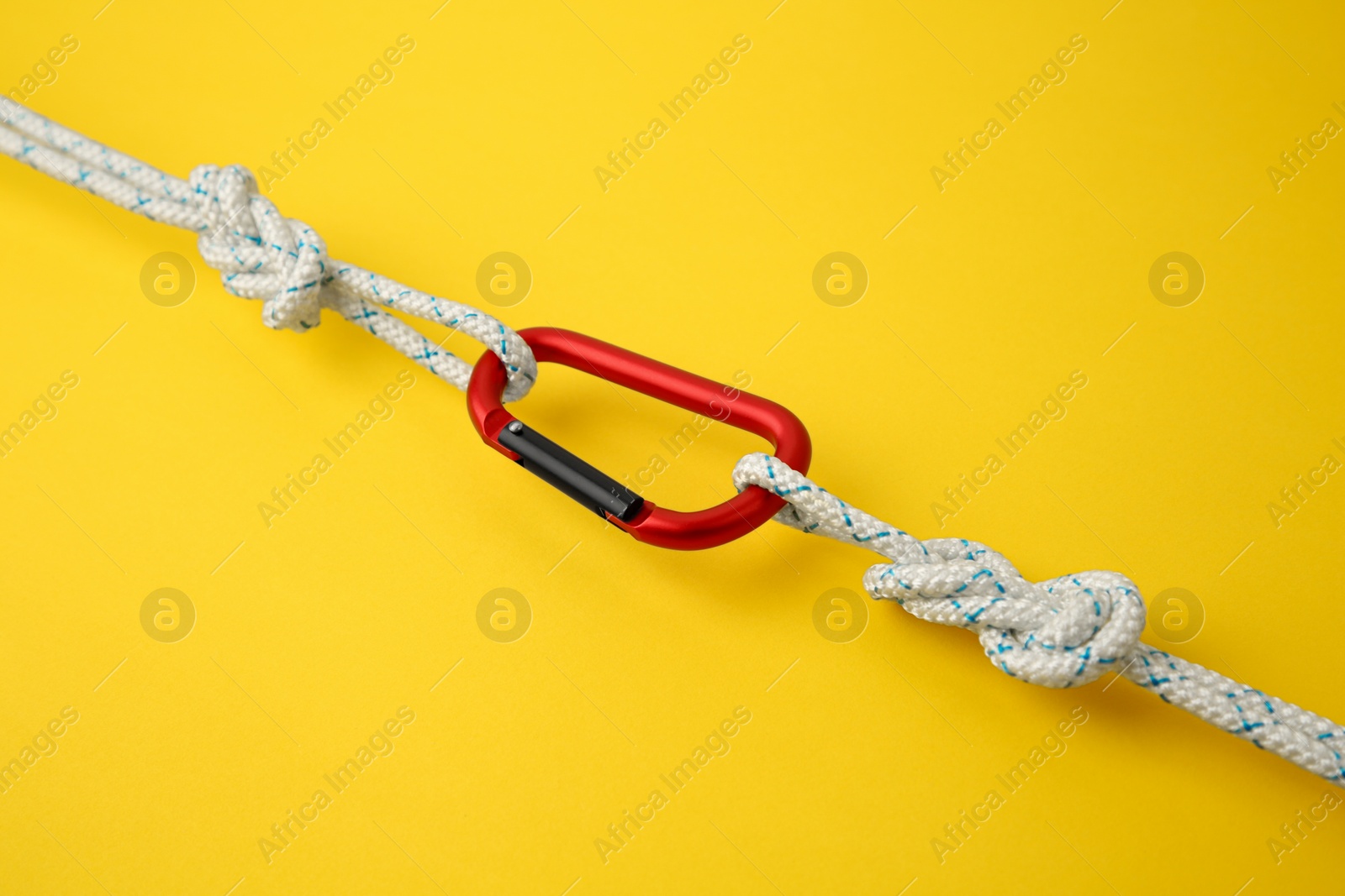 Photo of One metal carabiner with ropes on yellow background