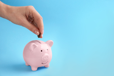 Photo of Woman putting coin into piggy bank on light blue background, closeup. Space for text