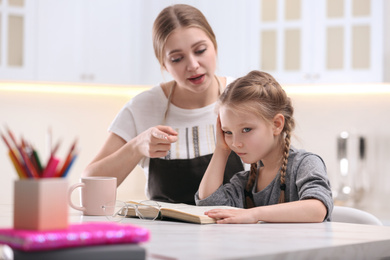 Photo of Woman helping her daughter with homework at table in kitchen