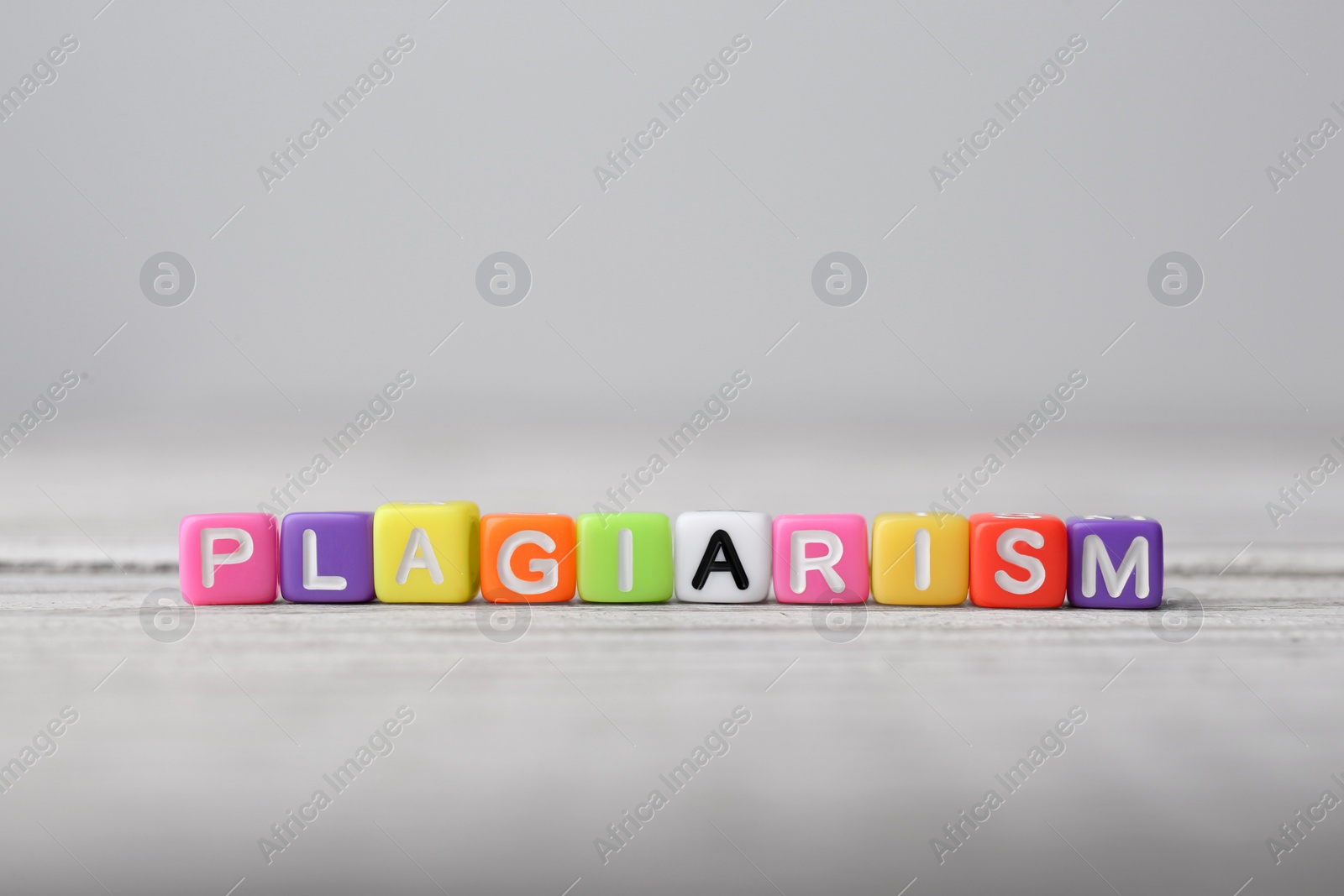 Photo of Colorful cubes with word Plagiarism on white wooden table