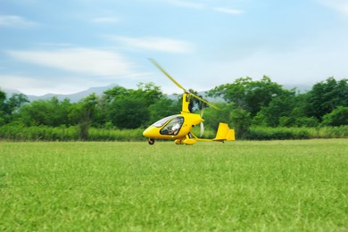 Photo of Yellow rotorcraft flying above grass near trees