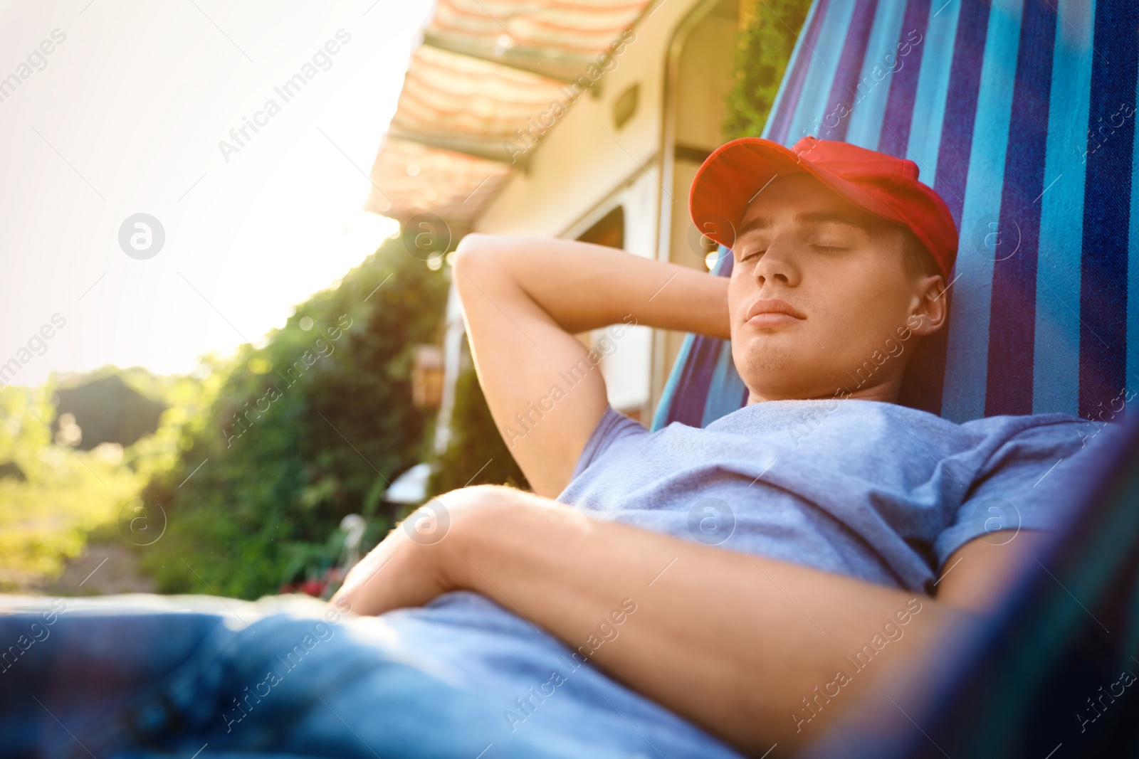 Photo of Young man resting in hammock near motorhome outdoors on sunny day