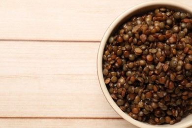 Photo of Delicious lentils in bowl on wooden table, top view. Space for text