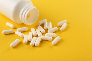 Bottle and vitamin capsules on yellow background, closeup. Space for text