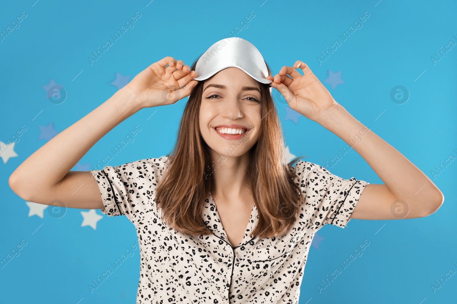 Photo of Beautiful woman wearing pajamas and sleep mask on light blue background. Bedtime