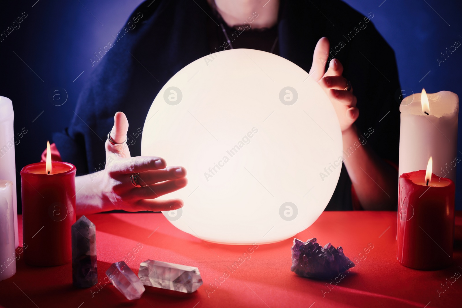 Photo of Soothsayer using glowing crystal ball to predict future  at table in darkness, closeup. Fortune telling