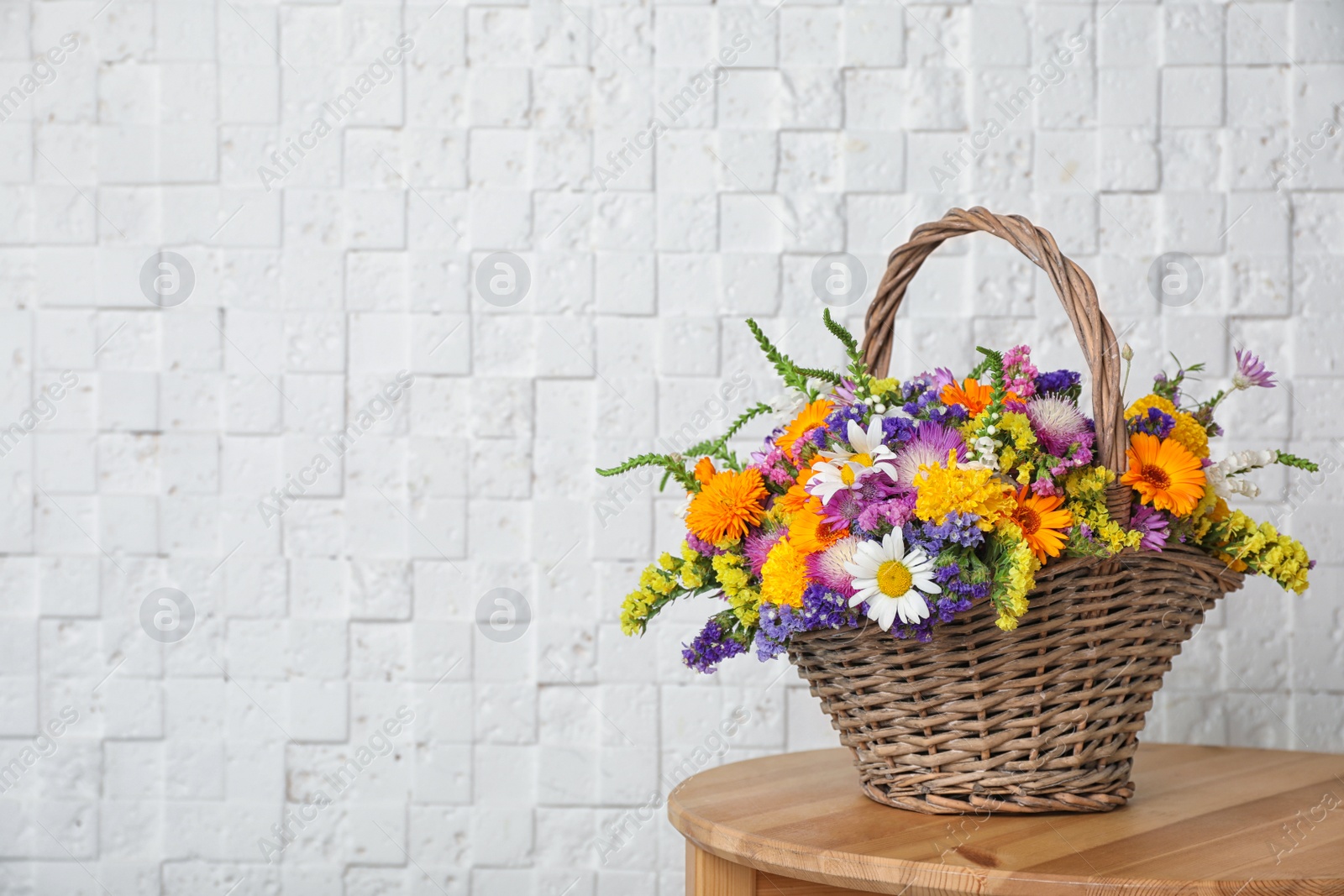 Photo of Wicker basket with beautiful wild flowers on table near white wall