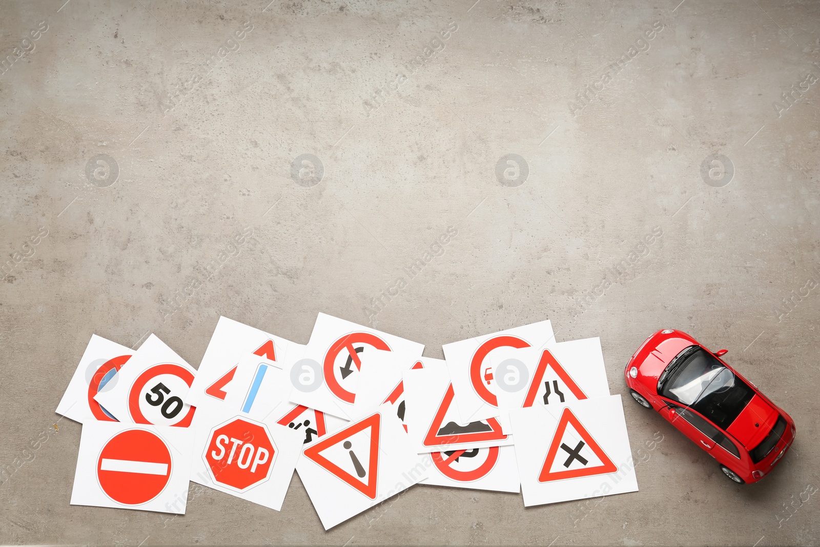 Photo of Many different road sign cards and toy car on grey table, flat lay with space for text. Driving school