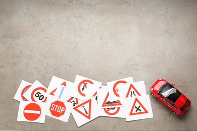 Many different road sign cards and toy car on grey table, flat lay with space for text. Driving school