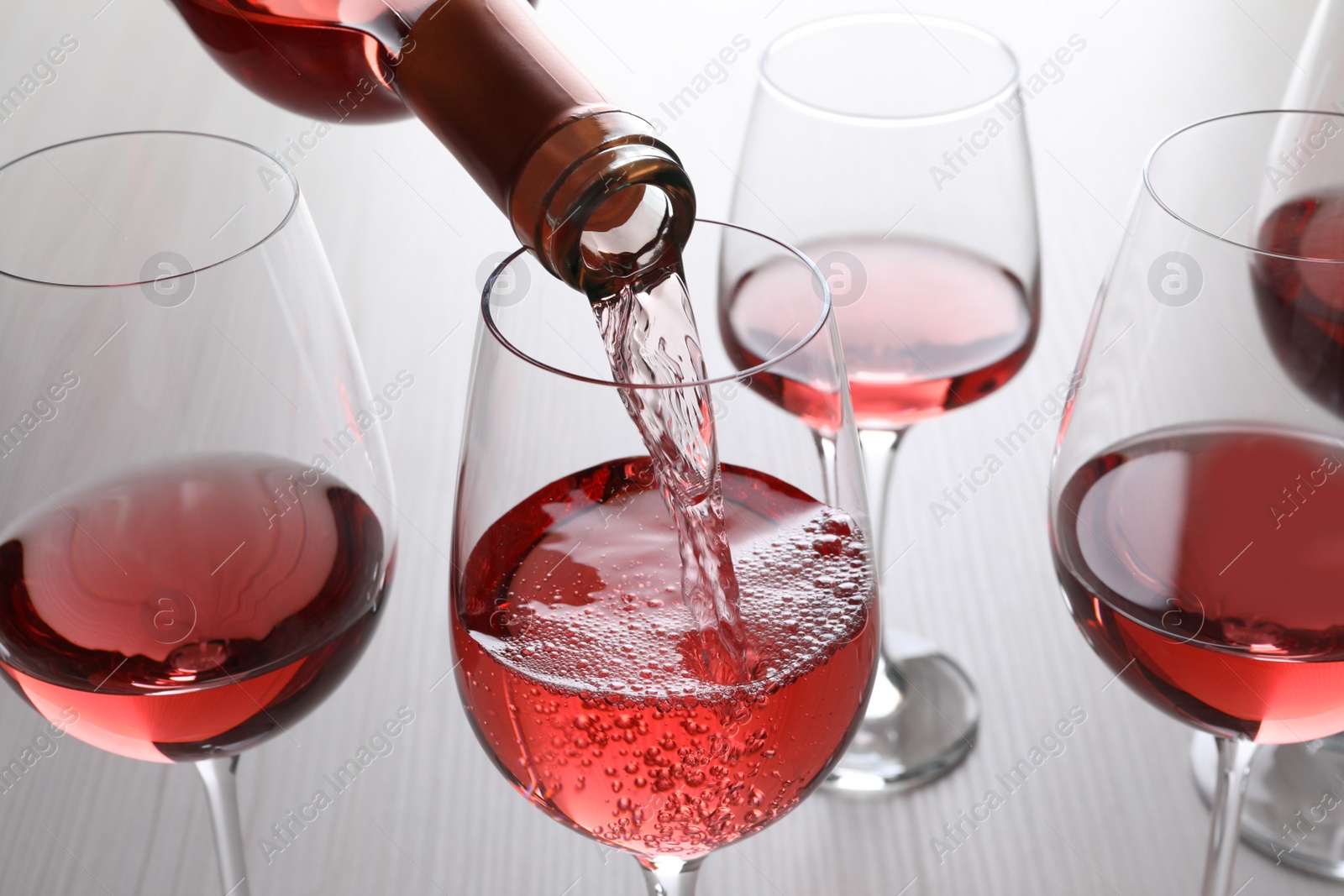 Photo of Pouring rose wine from bottle into glasses on wooden table, closeup